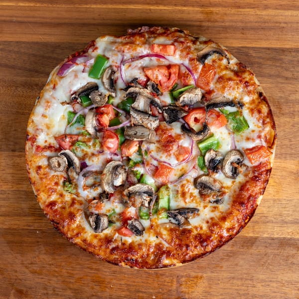 Round vegetable pizza with mushrooms, bell peppers, red onions, and tomatoes on a wooden background.