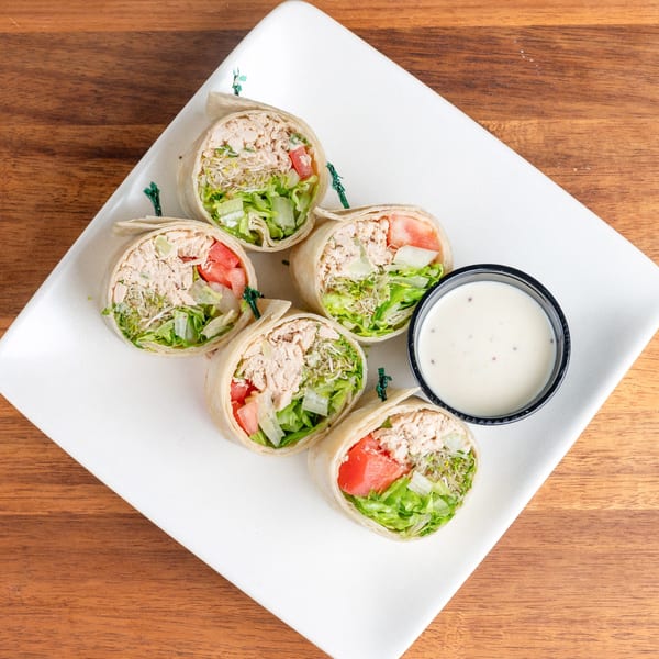 Five tuna salad wraps with lettuce, tomato, and sprouts, served with a side of dressing.