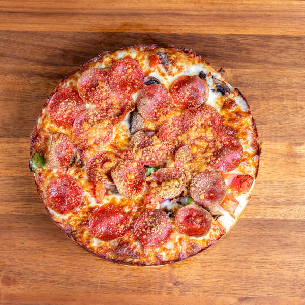 Overhead view of a whole pepperoni pizza with melted cheese and vegetables on a wooden table.