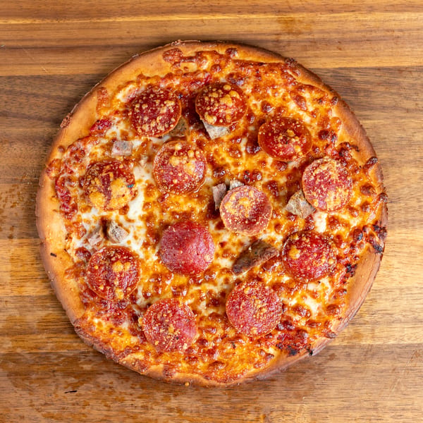 Round pizza with pepperoni and sausage on a wooden table.