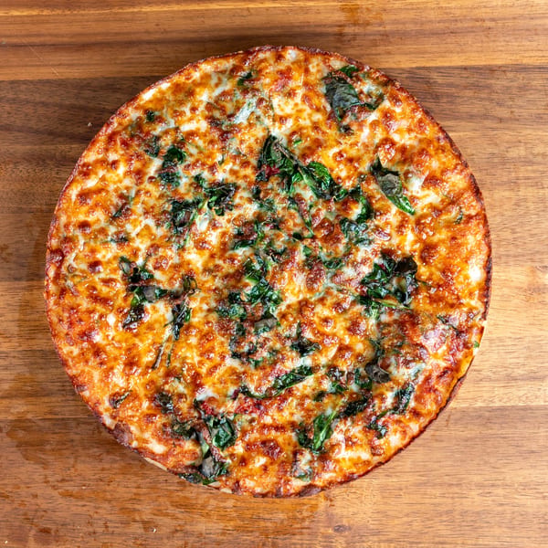 Overhead view of a whole pizza with melted cheese, spinach, and mushrooms on wood.