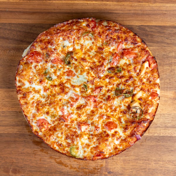 A whole pizza with melted cheese, tomatoes, and green peppers on a wooden surface.