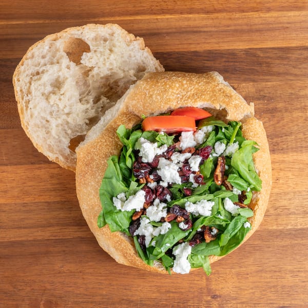 Bread bowl salad with spinach, feta, cranberries, pecans, and tomatoes on a wooden table.