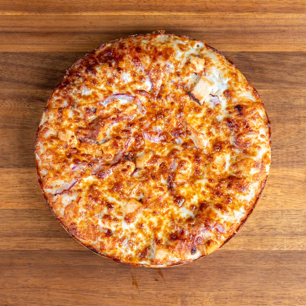 Golden brown pizza with melted cheese, chicken, and red onions on a wooden surface.