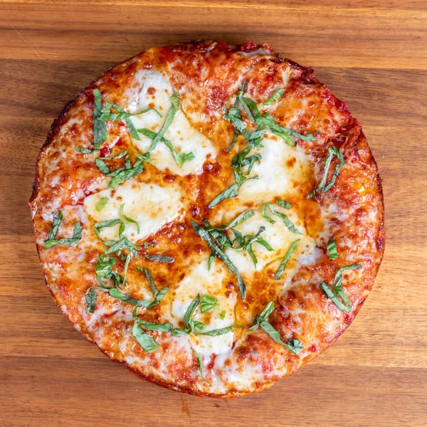 Margherita pizza with melted mozzarella, tomato sauce, and basil on a wooden surface.